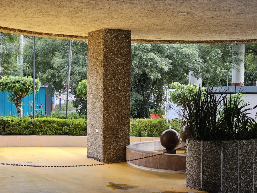 Llegada techada del hotel, con piso amarillo, una columna de piedra y la fuente de esferas al fondo